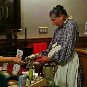 Dr. Florence K. Williams presents recreated artifacts to attendees. Items included slippers, a brandy bottle, faurina packets, and lemonade mix, which used the same recipe still used today.
